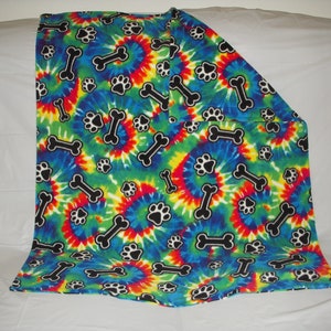 May include: A colorful tie-dye fleece blanket with a pattern of black paw prints and bones. The blanket is blue, green, yellow, orange, and red.