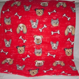 May include: Red fleece blanket with a repeating pattern of dog faces and bone shapes. The dogs are all different breeds and have various expressions.