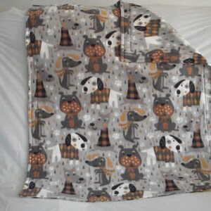May include: A gray fleece blanket with a pattern of dogs wearing scarves and hats. The dogs are in various colors, including brown, white, and black.