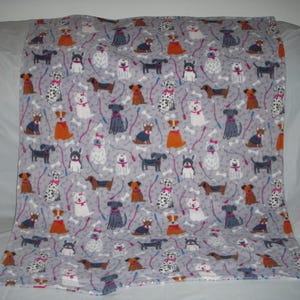 May include: A gray fleece blanket with a repeating pattern of colorful dogs on leashes. The dogs are all different breeds and have different colored collars. The background is a light gray with white bone-shaped designs.