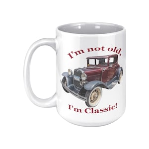 May include: White ceramic mug featuring a maroon vintage car illustration with the text "I'm not old, I'm Classic!" in maroon. The car has gray fenders and white-walled tires. The mug has a large handle.