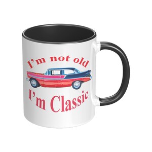 May include: White ceramic mug with a black rim and handle. The mug features a red and black vintage car with the text "I'm not old I'm Classic" in red.