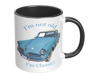 May include: White ceramic mug with a black rim and handle. The mug features a blue vintage car with a white roof and the text "I'm not old I'm Classic!"