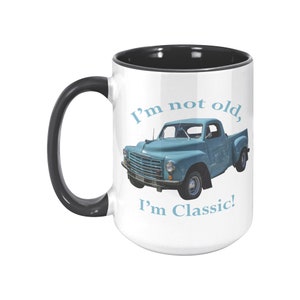 May include: A white ceramic mug with a black rim and handle. The mug features a blue vintage pickup truck with the text "I'm not old, I'm Classic!" in blue.