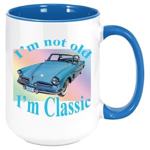 May include: White ceramic mug with a blue rim and handle. The mug features a blue 1953 car with the text "I'm not old I'm Classic" in blue.