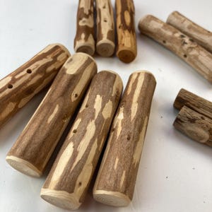 Pode incluir: Um conjunto de oito paus de madeira com um padrão natural de casca marrom e branca. Os paus têm furos perfurados e são de diferentes comprimentos.