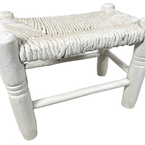May include: White wooden stool with a woven rush seat. The stool has turned legs and a simple design.