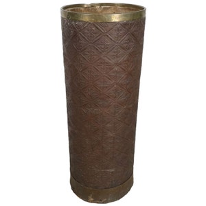 May include: A tall, brown, cylindrical umbrella stand with a brass top and bottom trim. The stand has a decorative embossed pattern.