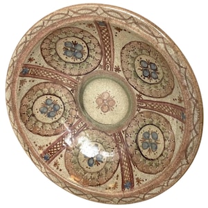 May include: A large, round ceramic bowl with a brown, beige, and blue design. The bowl has a raised rim and a center depression. The design features a repeating pattern of circles and swirls.