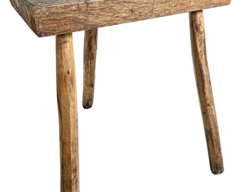 May include: A rustic, wooden stool with a weathered, octagonal top and three sturdy, tapered legs. The natural wood tones range from light tan to medium brown, showcasing the grain and texture of the material. The stool's design suggests a handcrafted, vintage aesthetic.