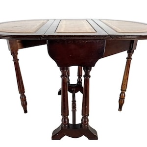 Op de afbeelding: Een ovale klaptafel van donkerbruin hout met een lederen blad. De tafel heeft vier poten met gedraaide spindels en een decoratieve basis.