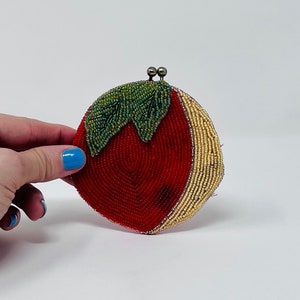 May include: A red and gold beaded purse shaped like a tomato with green beaded leaves.