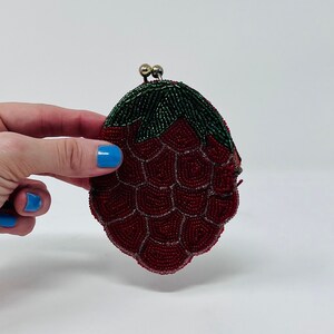 May include: A red beaded coin purse shaped like a strawberry with green leaves.