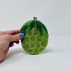 May include: A green beaded clutch purse shaped like a pineapple with a silver clasp.