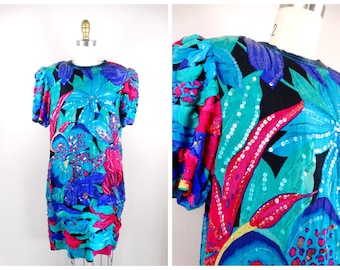 May include: A sequined dress with a floral design in turquoise, fuchsia, and blue. The dress has short, puffed sleeves and a ruched hem. Black accents enhance the bold, colourful look. The dress is displayed on a mannequin.