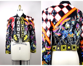 May include: A black sequined jacket with a colorful geometric and floral design. The jacket has a  "COLLAPSIBLE SHOULDER" label and the number "2" on the front.