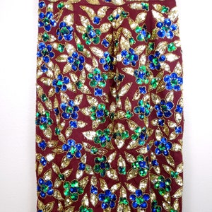 Puede incluir: Una falda color burdeos con un estampado floral hecho de lentejuelas doradas, azules y verdes.