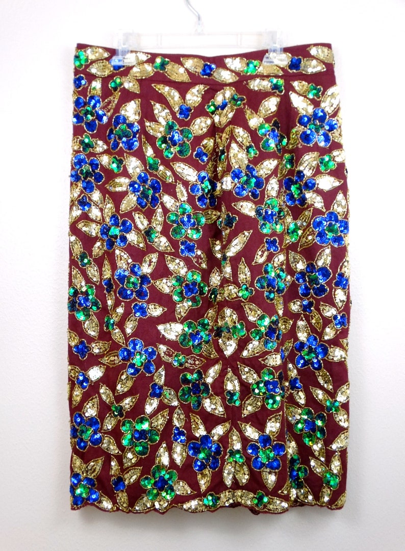 Puede incluir: Una falda color burdeos con un estampado floral hecho de lentejuelas doradas, azules y verdes.