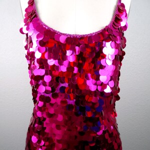 May include: A vibrant, fuchsia sequin dress with spaghetti straps. The dress is covered in overlapping, circular sequins that catch the light, creating a shimmering effect. The neckline and straps are a darker shade of pink.