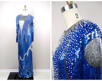 May include: A long, blue and silver sequined dress with a geometric pattern. The dress has a round neckline and long sleeves. The dress is decorated with white pearls.