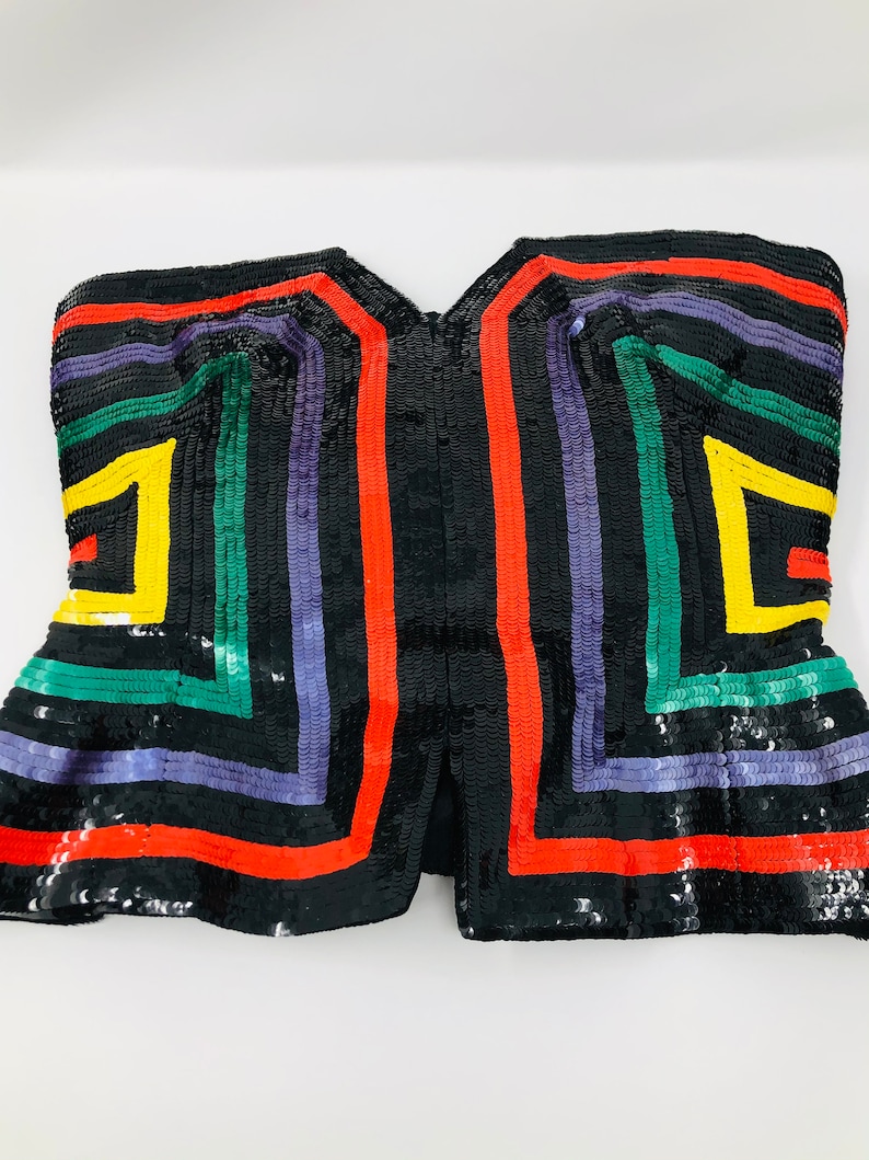 May include: A black sequined strapless top with a geometric pattern in red, yellow, green, and purple.