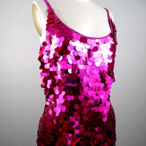May include: A sleeveless, fuchsia sequin dress on a mannequin. The dress features a scoop neckline and thin straps. The sequins are circular and cascade down the dress, creating a shimmering effect. The dress is a vibrant shade of pink.