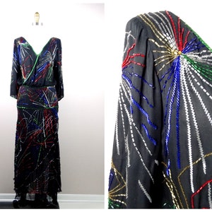 May include: A black long-sleeved dress with a V-neckline and a colorful beaded design. The beads are arranged in a geometric pattern that resembles fireworks.