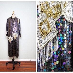 May include: A long, sequined dress with long sleeves and a high collar. The dress is primarily black with iridescent sequins and features ornate gold and silver beaded embellishments on the shoulders and bodice. Two decorative fan-shaped appliqués are on the front.