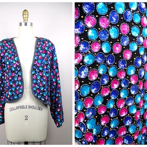 May include: A cropped sequined jacket with a collapsible shoulder design. The jacket is black with blue and pink sequins arranged in a circular pattern.
