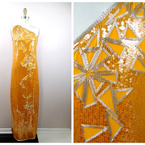 K&ouml;nnte beinhalten: Ein langes, einarmige Kleid in leuchtend gelber Farbe. Das Kleid ist mit Pailletten besetzt und hat ein geometrisches Muster aus silbernen Pailletten.