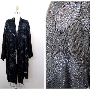 Könnte beinhalten: Eine lange schwarze Paillettenjacke mit V-Ausschnitt und langen Ärmeln. Die Jacke besteht aus verschiedenen Pailletten und Perlen, die einen strukturierten und schillernden Look erzeugen.