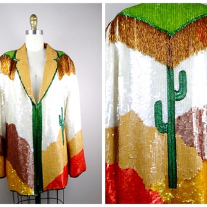 May include: A white sequined jacket with a desert landscape design. The jacket features a green cactus, brown mountains, and gold and red accents. The jacket has a green zipper and a gold fringe collar.