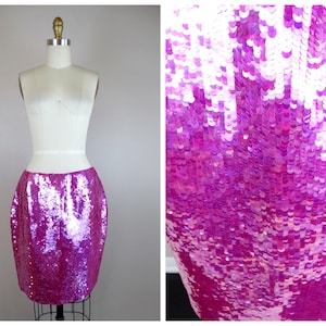 May include: A pink sequined skirt with a high waist and a fitted silhouette. The skirt is made of iridescent sequins that shimmer in the light.