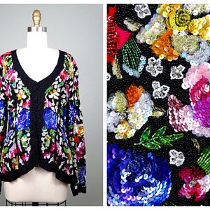 Pode incluir: Um casaco preto com um padr&atilde;o floral feito de lantejoulas e contas. O casaco tem um decote em V e mangas compridas. As flores s&atilde;o em tons de rosa, azul, verde, amarelo e laranja.