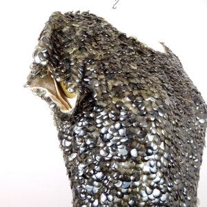 May include: A close-up of a garment made of overlapping, iridescent, grey, plastic scales. The garment is on a dress form.