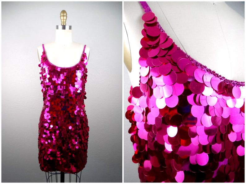 May include: A vibrant fuchsia sequin dress with thin straps. The dress is covered in large, round sequins that catch the light, creating a shimmering effect. The dress is displayed on a mannequin, showcasing its form-fitting design.