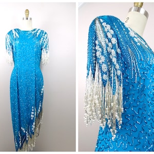 May include: A turquoise sequined dress with white beaded fringe on the sleeves and hem. The dress has a fitted bodice and a flowing skirt.