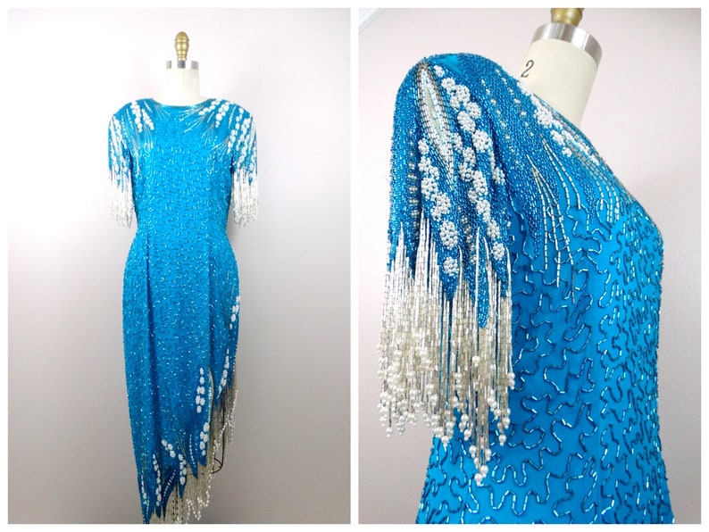 May include: A turquoise sequined dress with white beaded fringe on the sleeves and hem. The dress has a fitted bodice and a flowing skirt.