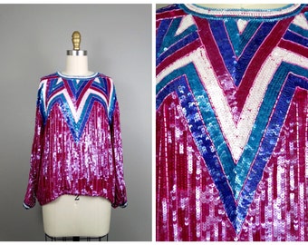 May include: A pink, blue, and white sequined top with a geometric pattern. The top has long sleeves and a round neckline.