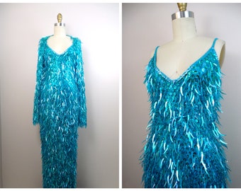 May include: A long turquoise sequined dress with a V-neckline and long sleeves. The dress is made of sequins that are arranged in a fringe-like pattern.