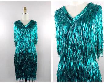 May include: A teal blue sequined dress with a V-neckline and short sleeves. The dress is covered in sequins that resemble fringe.