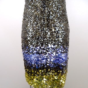 May include: A sequined dress with a silver, purple and gold colour scheme. The dress is made of small, overlapping sequins that create a shimmering effect.