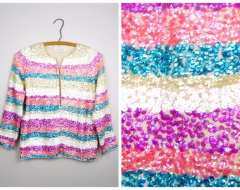May include: A white sequined jacket with horizontal stripes of pink, blue, and white. The jacket has a zipper closure and long sleeves.