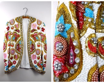 May include: A white jacket with a paisley pattern, embellished with colorful beads, sequins, and rhinestones. The jacket has a shawl collar and long sleeves.