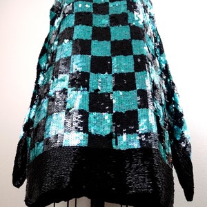 Puede incluir: Una blusa de lentejuelas negra y turquesa con un patr&oacute;n de cuadros. La blusa tiene mangas largas y un corte holgado.
