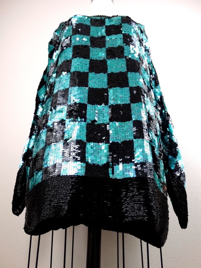 Puede incluir: Una blusa de lentejuelas negra y turquesa con un patr&oacute;n de cuadros. La blusa tiene mangas largas y un corte holgado.