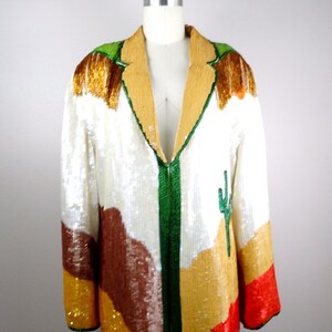 May include: A white sequined jacket with a green, brown, orange, and red desert landscape design. The jacket has a v-neck and a front zipper closure.