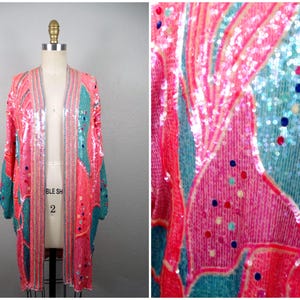 Peut inclure: Un kimono long en sequins rose et turquoise avec un motif géométrique. Le kimono a un col en V et des manches longues.