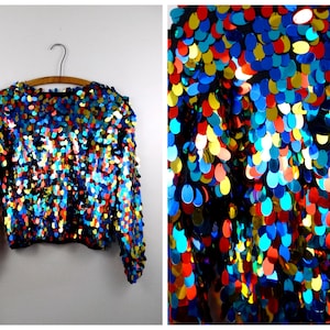 May include: A long-sleeved, cropped top covered in iridescent sequins in shades of blue, red, yellow, and gold.