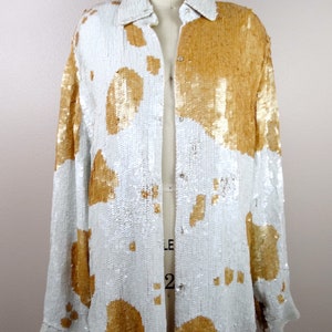 May include: A white and gold sequined button-up shirt with a long sleeve and a collared neckline.
